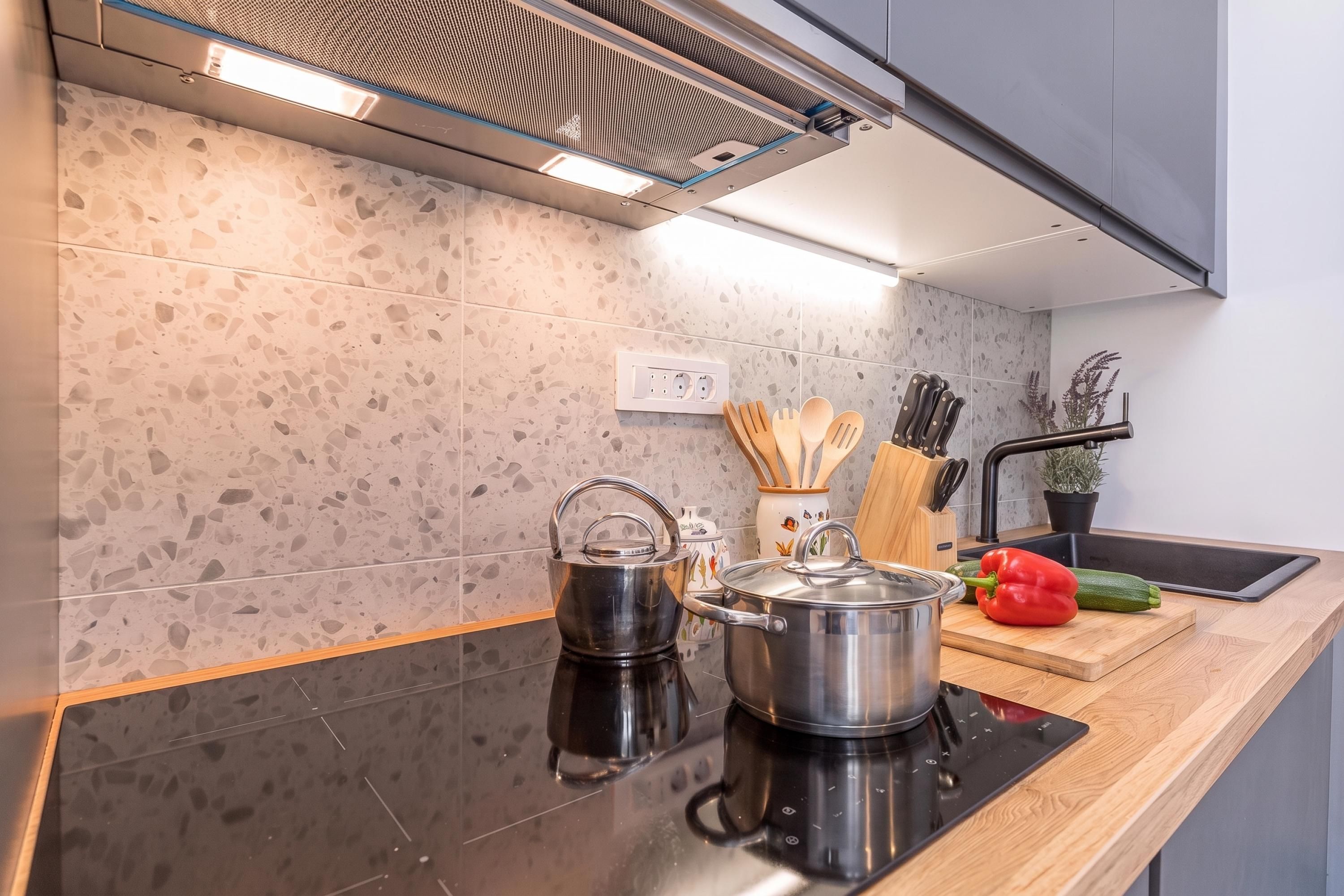Een moderne keuken met een zwart aanrecht, een roestvrijstalen waterkoker, pan en een rode paprika.
