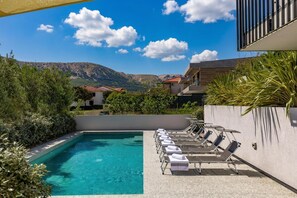 Une piscine entourée de chaises longues, de verdure et offrant une vue sur la montagne.
