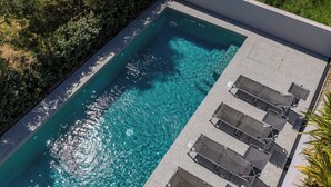 An aerial view of a rectangular swimming pool with clear blue water, surrounded by a paved deck and a row of sun loungers. - Pool Apartment Sapore Di Mare 1, Baška, Croatia (Baška)