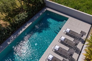 Une piscine rectangulaire à l’eau d’un bleu limpide, entourée d’un petit muret et d’une zone herbeuse.
