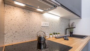 A modern kitchen with a black induction cooktop, a stainless steel kettle, and a wooden countertop. - Pool Apartment Sapore Di Mare 1, Baška, Croatia (Baška)