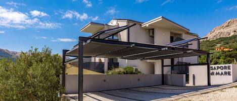 A modern two-story house with a covered outdoor area, solar panels, and a sign reading 'Sapore del Mare'.