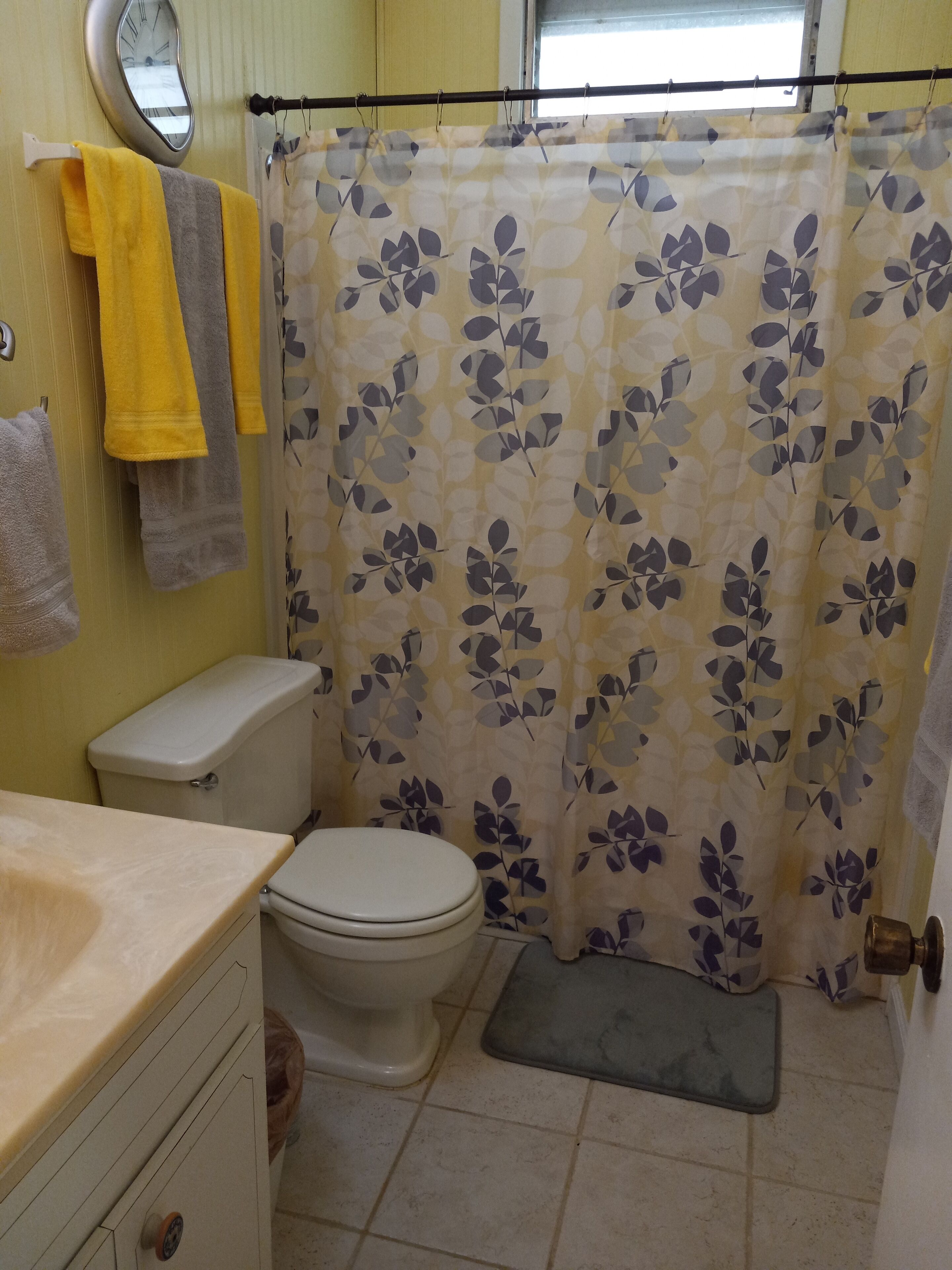 Un bagno con il water, un lavandino, una tenda da doccia con motivo a foglia e asciugamani appesi al muro.