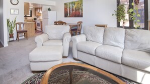 A living room with a white leather sofa, a coffee table, and a dining area with wooden chairs. There is a kitchen in the background with a refrigerator and a microwave. - West Vail Riverfront Lodging, Colorado (Vail)