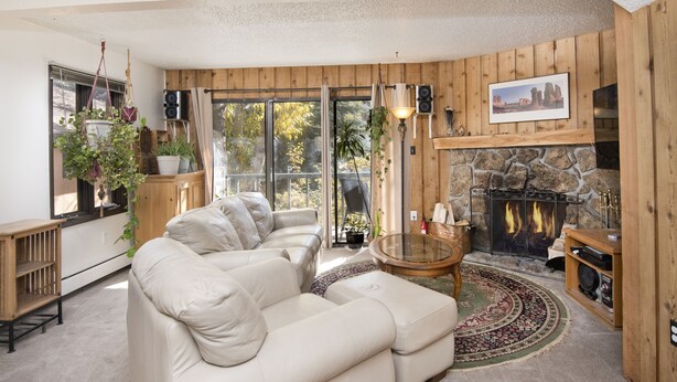 A cozy living room with a stone fireplace, a beige leather sofa, and a large window with curtains. - West Vail Riverfront Lodging, Colorado (Vail)