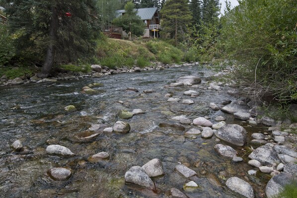 Un río con rocas y una casa al fondo.