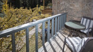 A wooden deck with a stone wall, a table, and two striped chairs. - West Vail Riverfront Lodging, Colorado (Vail)