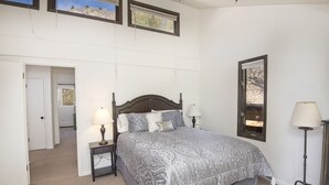 A bedroom with a large bed, two bedside tables with lamps, a door, and a window with a view of trees. - West Vail Riverfront Lodging, Colorado (Vail)