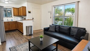 A modern living room with a black leather sofa, a coffee table, and a kitchen area with wooden cabinets and a stainless steel refrigerator. - Grand Canyon Basecamp with EV (Williams)