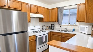 A kitchen with wooden cabinets, a stainless steel refrigerator, a gas stove, an oven, a microwave, and a sink. - Grand Canyon Basecamp with EV (Williams)
