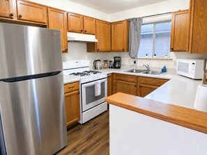 Una cocina con armarios de madera, un refrigerador de acero inoxidable, una estufa a gas, un horno, un microondas y un fregadero.