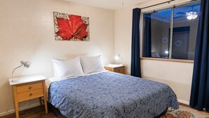 A bedroom with a bed, nightstands, a lamp, a window with curtains, and a wall-mounted artwork. - Grand Canyon Basecamp with EV (Williams)