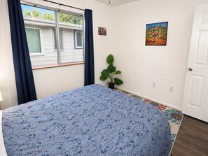 A bedroom with a bed, a window with curtains, a potted plant, and a door. - Grand Canyon Basecamp with EV (Williams)