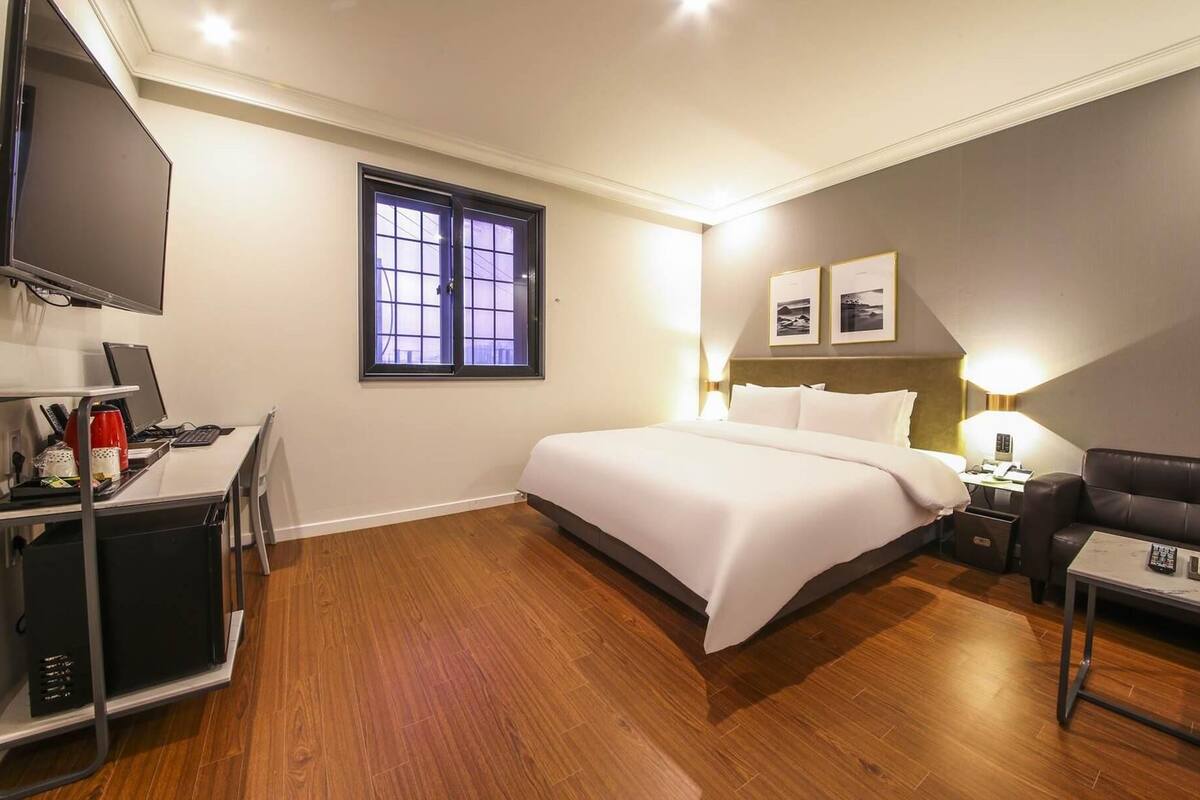 Ein Hotelzimmer mit Bett, Schreibtisch mit Computer, Fernseher, Fenster und einer Couch.