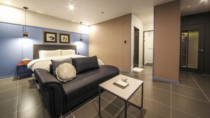 A modern hotel room with a bed, a sofa, a small table, and a bathroom visible through a glass door. - Gupo Brown-Dot Hotel (Busan)