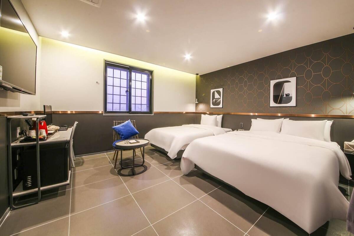 Ein Hotelzimmer mit zwei Betten, einem Schreibtisch, einem Stuhl, einem kleinen Tisch und einem Fenster.