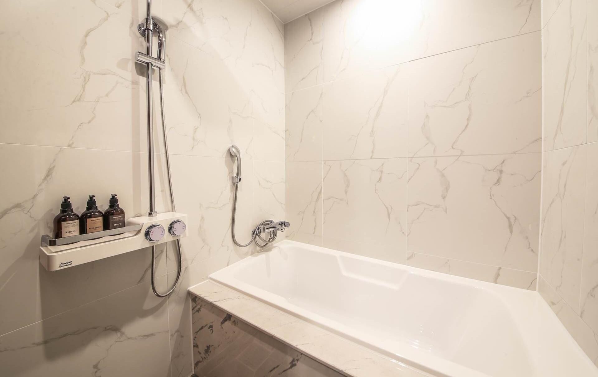 A bathroom with a bathtub, a shower, and a shelf with toiletries.