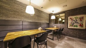A restaurant interior with a brick wall, cushioned bench seating, wooden tables, black chairs, pendant lighting, and a framed artwork on the wall. - Gupo Brown-Dot Hotel (Busan)