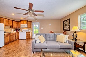 A compact living space with a kitchenette, a grey sofa, a glass coffee table, and a ceiling fan. - K&M Lake Rentals Cabin #1 (Burkeville)