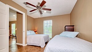 A bedroom with two beds, a ceiling fan, and a window with blinds.