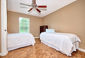 A bedroom with two beds, a ceiling fan, a window with blinds, and a wooden dresser.