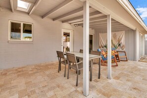 Un patio cubierto con una mesa y sillas de comedor, un muro de ladrillo blanco y vista al cielo.