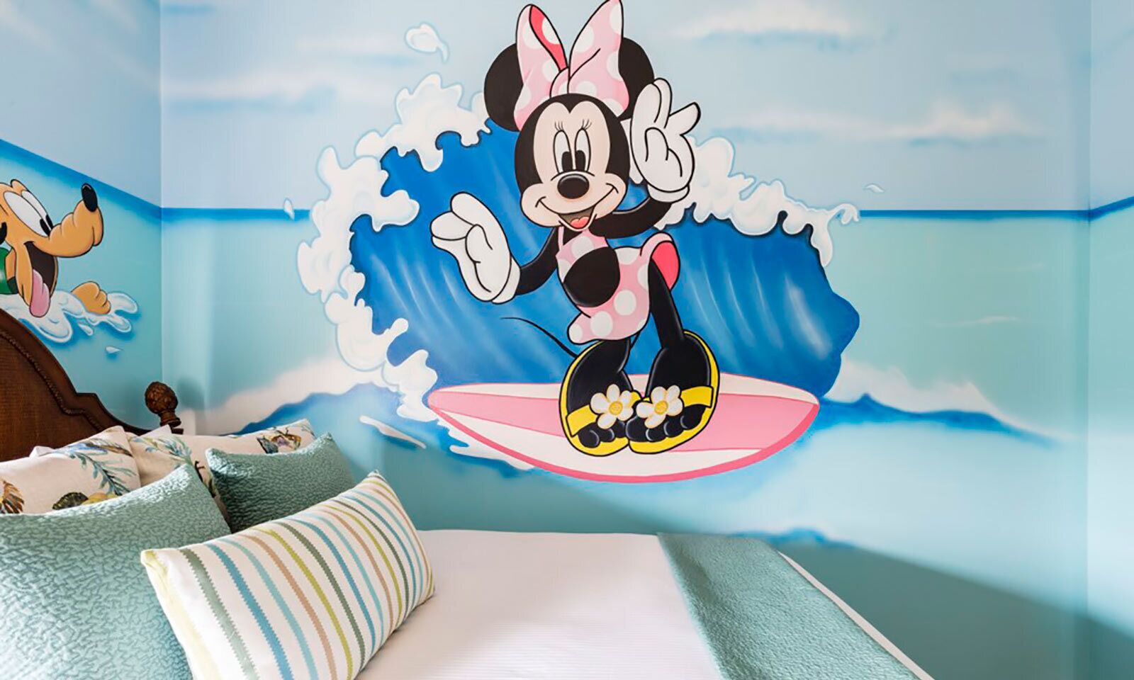 Ein Zimmer mit Wandgemälde einer Zeichentrickfigur, einem Bett mit gestreiftem Kopfkissen und einem Holz-Kopfteil.