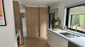 A modern kitchen with wooden cabinets, a built-in oven, a sink, and a window with a view of greenery. - Welcome to Rose on Rye, your private oasis.<br> (Rye)