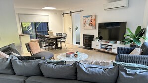 A modern living room with a grey sofa, a dining area with a table and chairs, a TV, and a bookshelf. - Welcome to Rose on Rye, your private oasis.<br> (Rye)