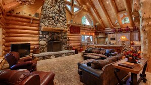 A log cabin interior with a stone fireplace, leather furniture, and a kitchen area.