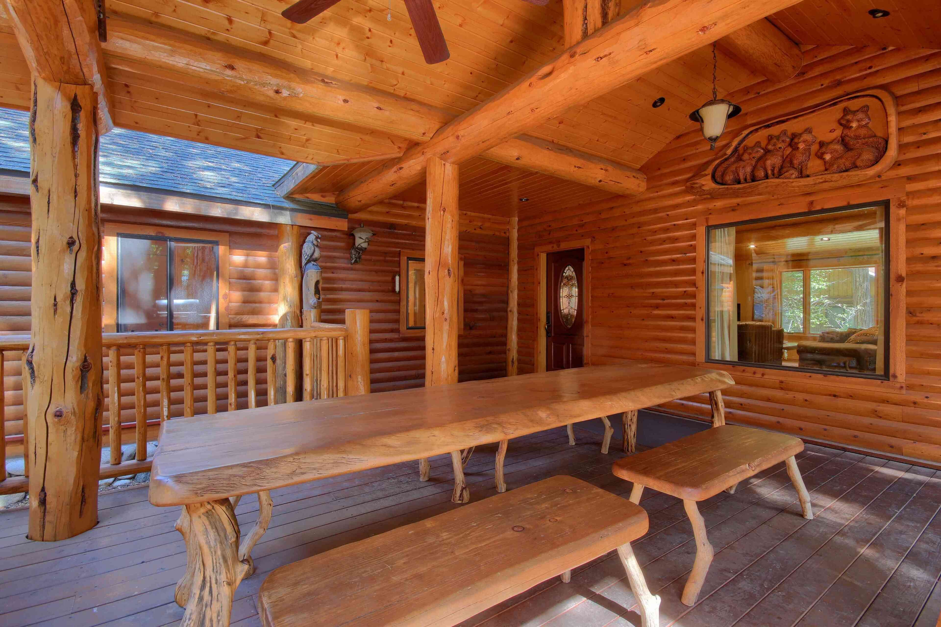 A wooden cabin interior with a large dining table, benches, and a wooden ceiling with a carved bear design.