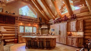 A log cabin with a large central island, wooden cabinets, and a stone fireplace.