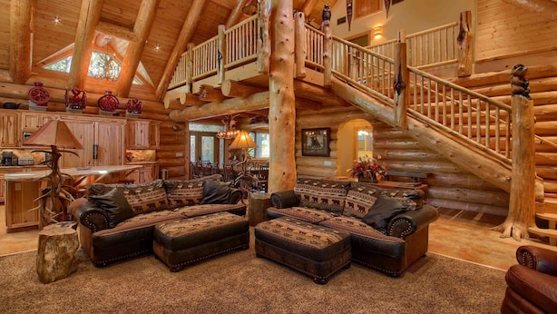 A log cabin interior with a large staircase, leather sofas, and a dining area.