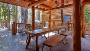 A wooden deck with a long table and benches, surrounded by trees.