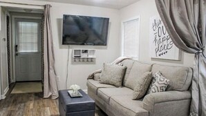 Una sala de estar con un sofá gris, un televisor de pantalla plana montado en la pared y una mesita auxiliar con un objeto decorativo.