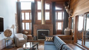 A spacious living room with a large sectional sofa, a glass coffee table, and a fireplace. There is a ceiling fan, a mounted deer head, and a large window providing natural light. - Stunning Eastern Sierra Retreat: 3 Bed+Loft/3 Baths, Spacious, Pet-Friendly (Mammoth Lakes)