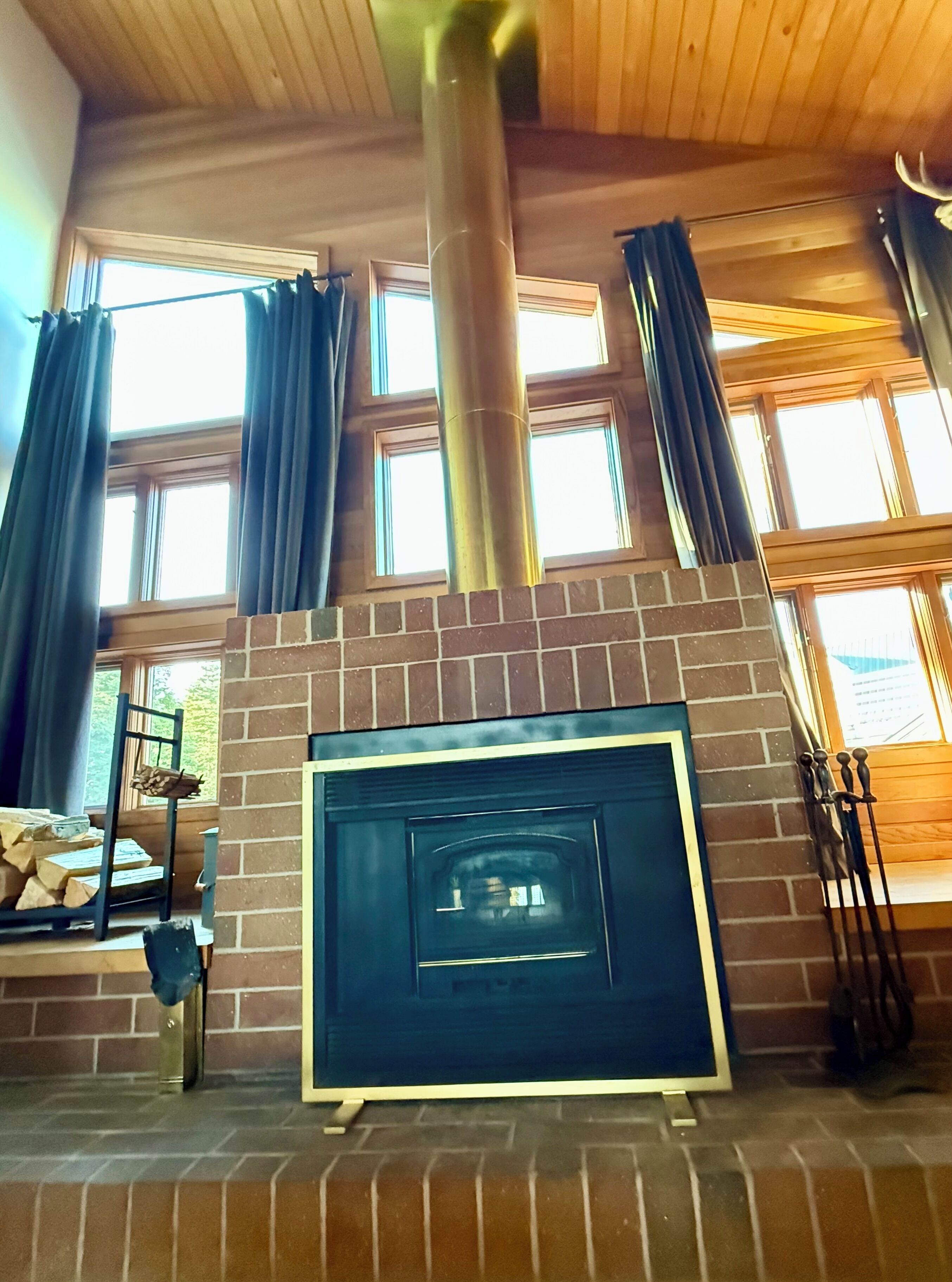 A fireplace with a metal frame, a brick wall, and a window with curtains.