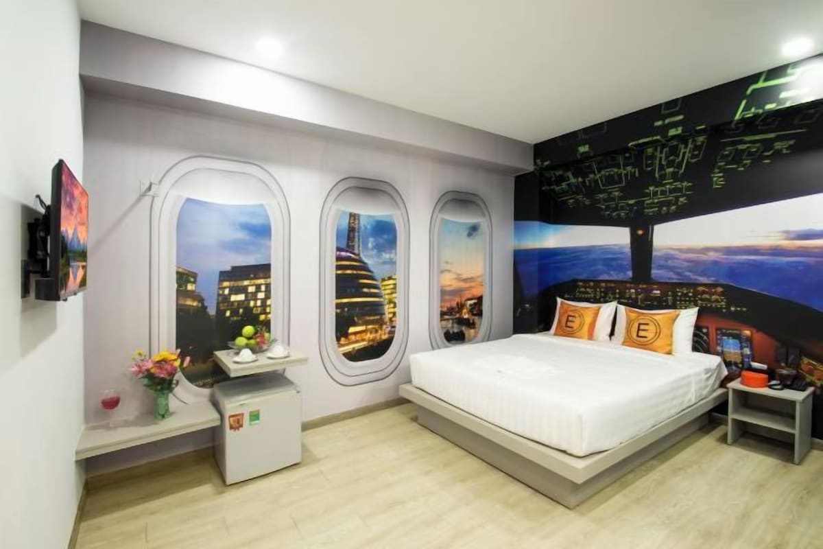 Habitación de hotel con cama, escritorio, silla, mesita y ventana con vista panorámica de la ciudad.
