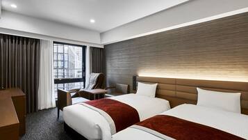 Habitación de hotel con dos camas, un escritorio, una silla y un ventanal grande.