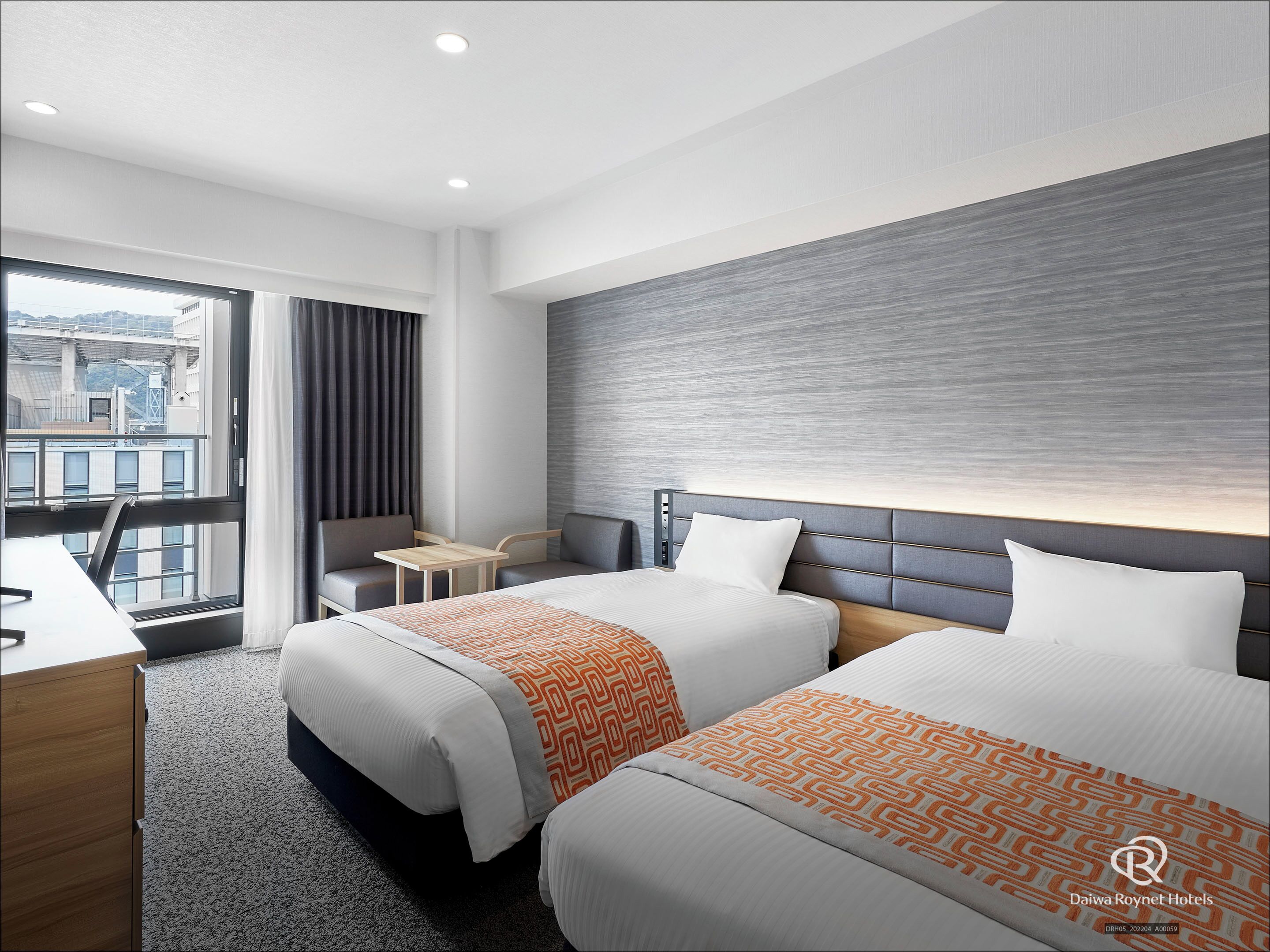Ein Hotelzimmer mit zwei Betten, einem Schreibtisch, einem Stuhl und Blick auf die Stadt.
