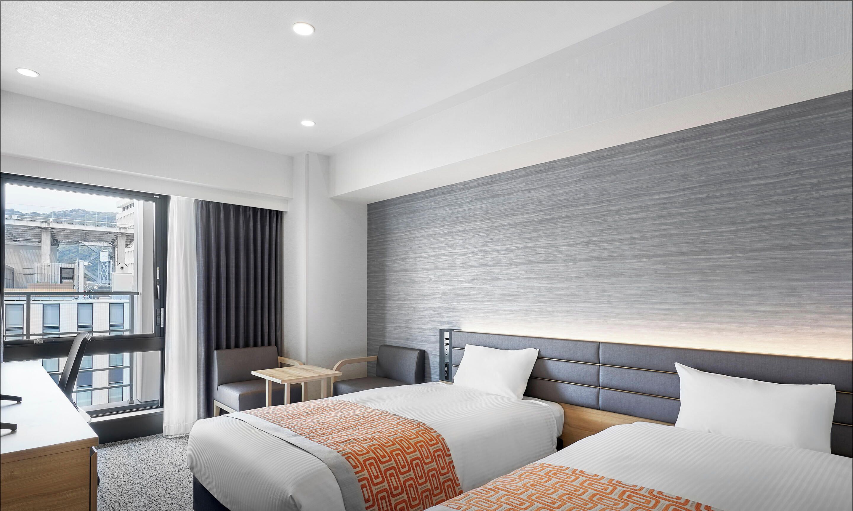 Ein Hotelzimmer mit zwei Betten, einem Schreibtisch, einem Stuhl und Blick auf die Stadt.