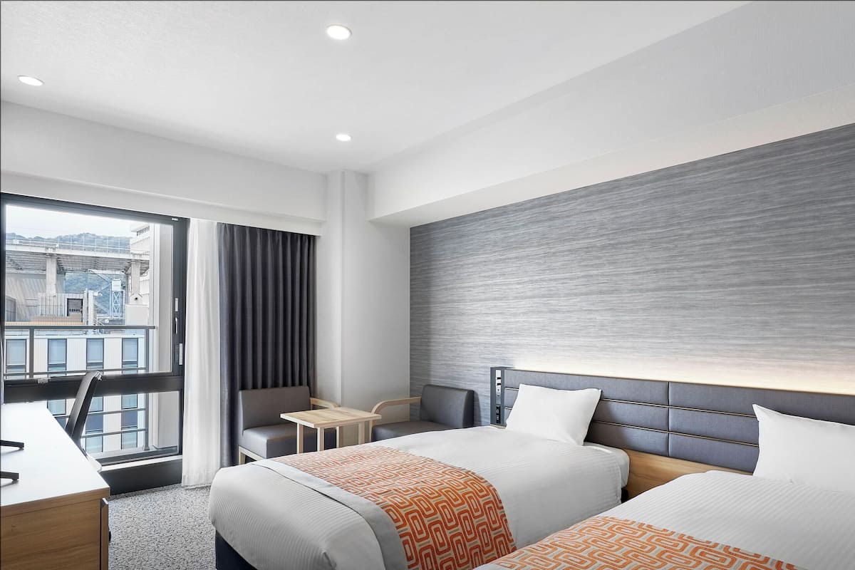 Une chambre d’hôtel avec deux lits, un bureau, une chaise et une vue sur la ville.