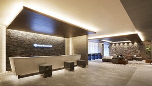 A modern hotel lobby with a reception desk, stone wall, and seating area.