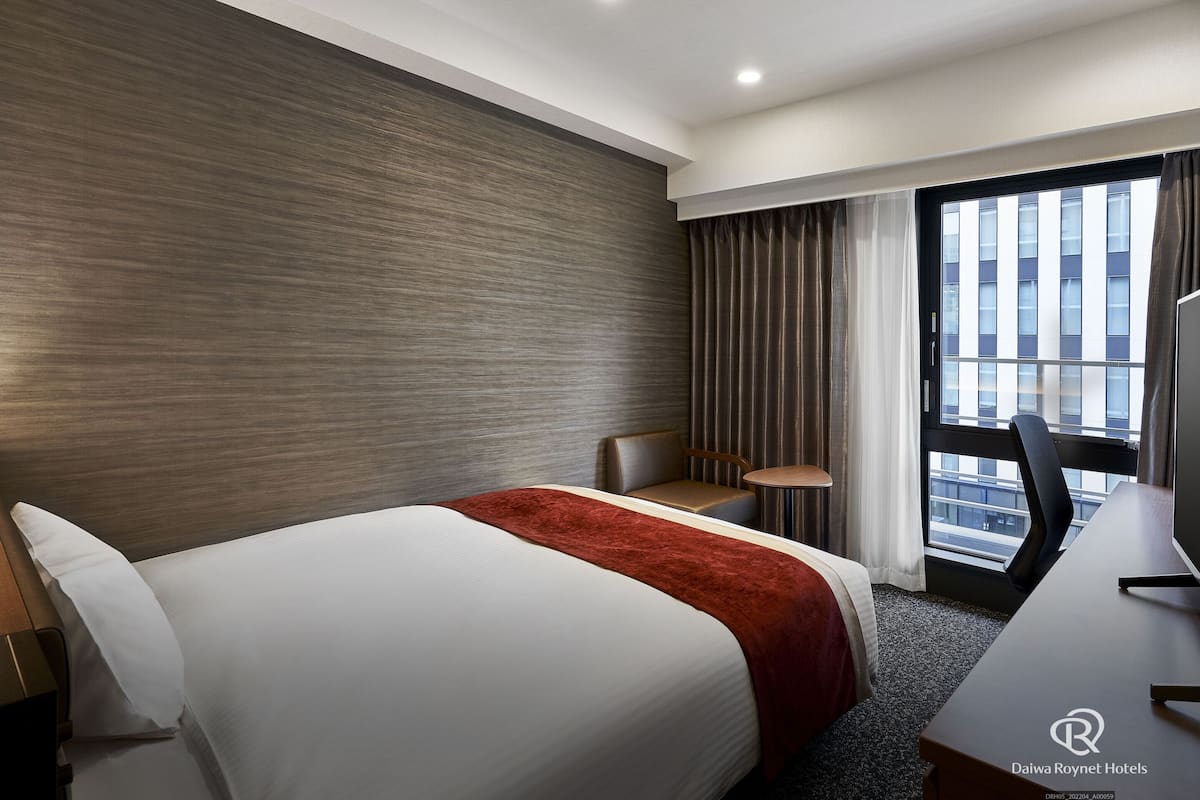 Une chambre d’hôtel avec un grand lit, un bureau, une chaise et une fenêtre avec des rideaux.