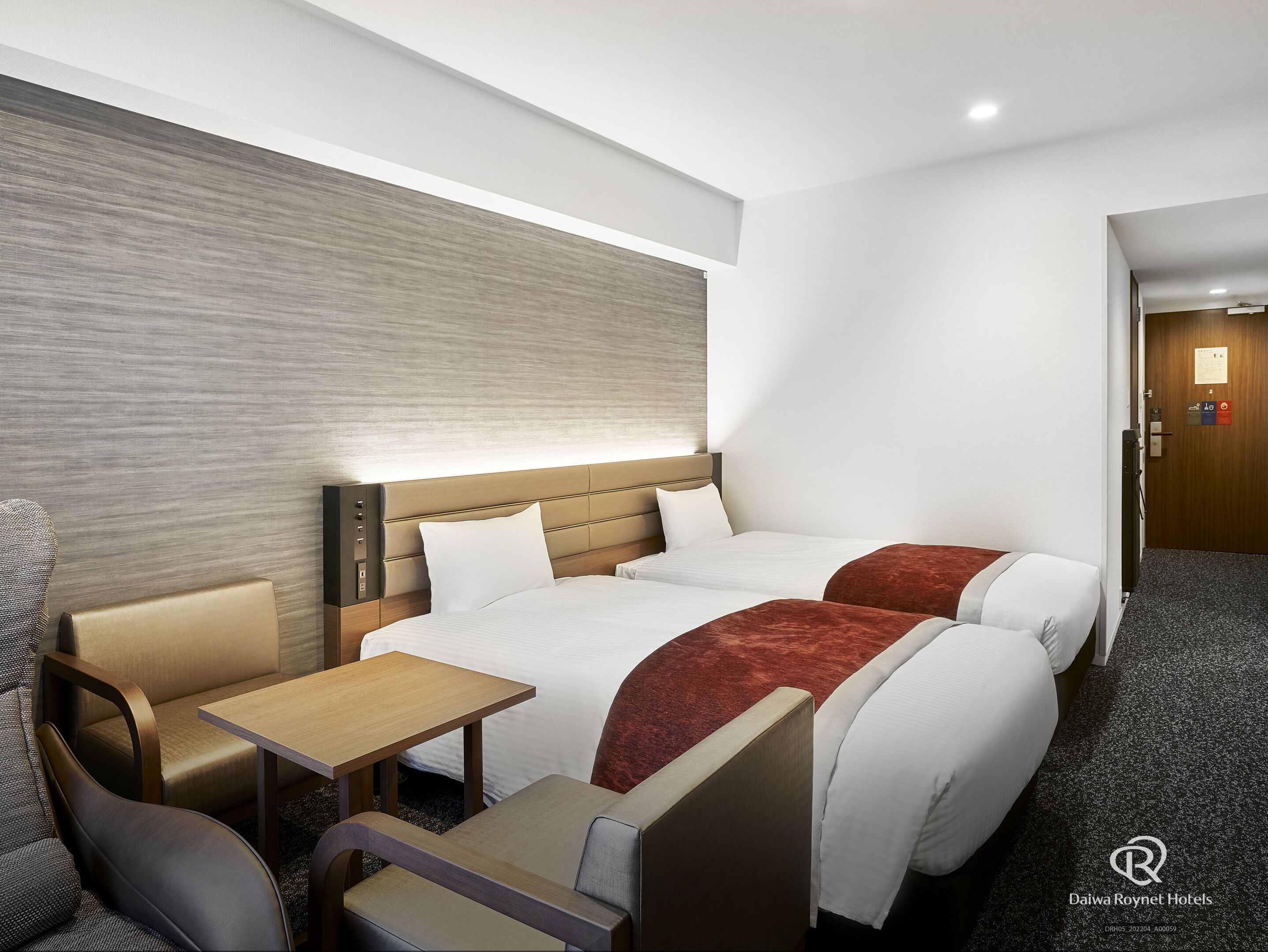 Ein Hotelzimmer mit zwei Betten, einem Schreibtisch und einem Stuhl.