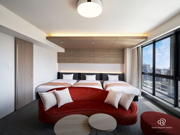 A modern hotel room with a large bed, a red sofa, and a city view.
