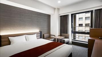 A hotel room with a large bed, a desk, a chair, and a view of the city.
