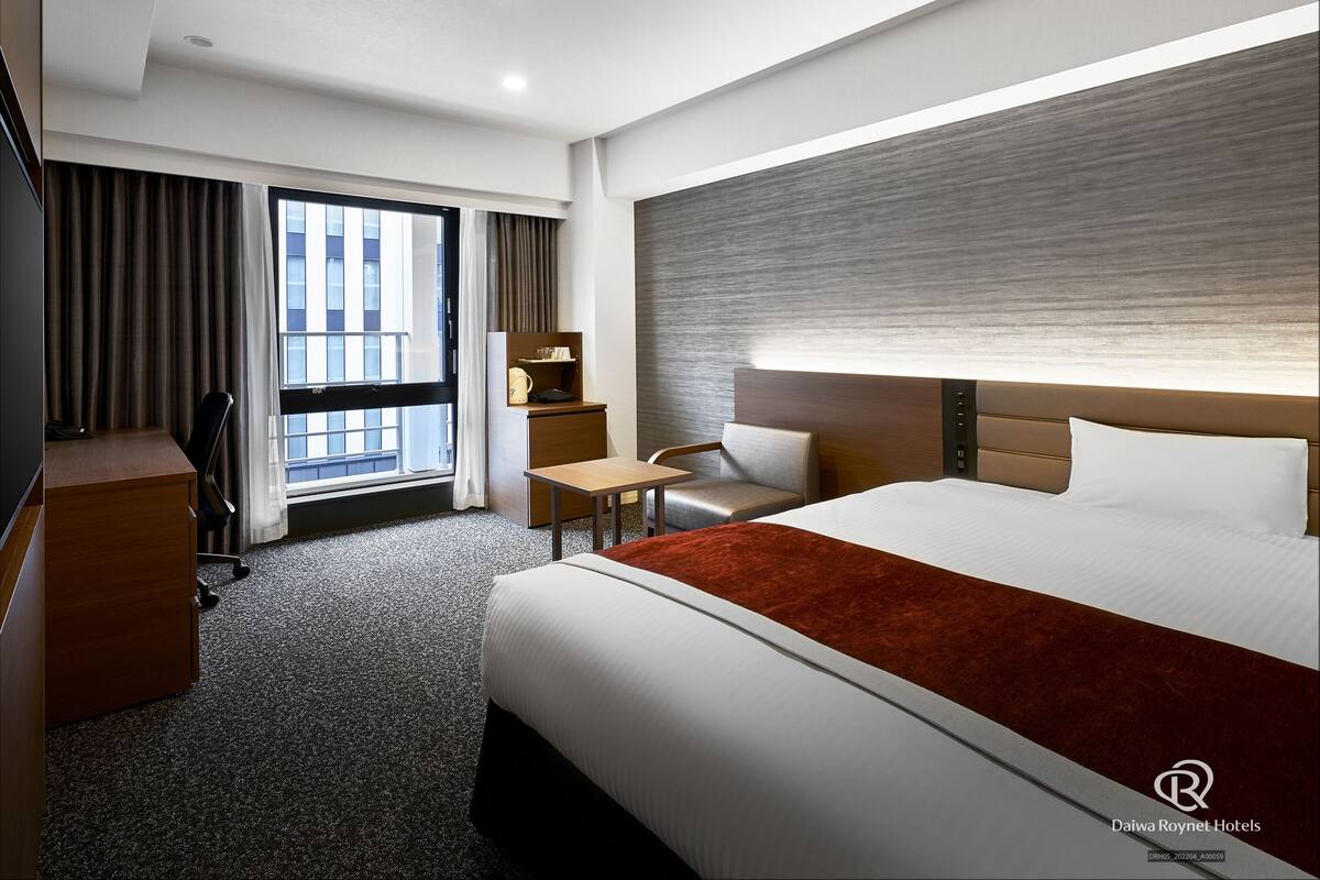 Une chambre d’hôtel avec un lit, un bureau, une chaise et une fenêtre avec des rideaux.