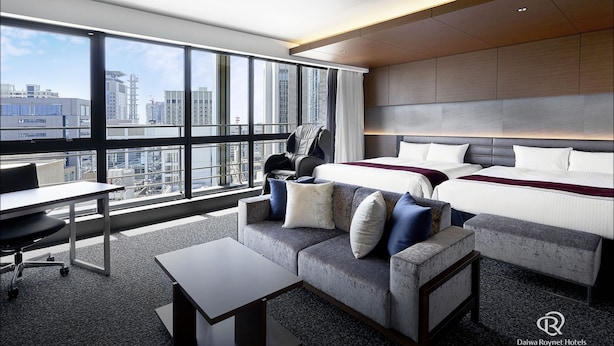 A modern hotel room with a large window, a bed, a sofa, a desk, and a chair.