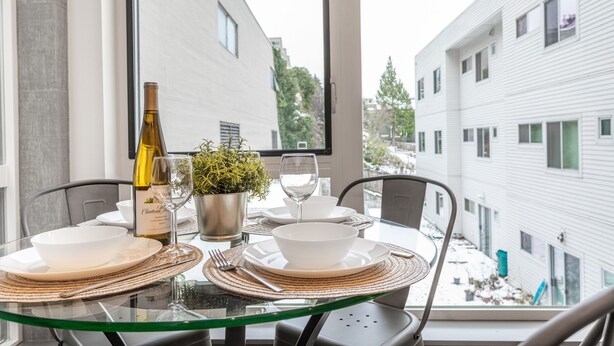 A dining table set with plates, bowls, cutlery, a wine bottle, and a glass, with a view of buildings through a window. - ⚡️The Brooklyn⚡️CENTRAL Capital Hill with Perfect Walking score🚶🏻‍♂️with Rooftop views (Seattle)